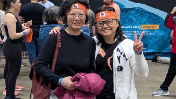 Two asian people smiling in the camera with sports clothes. One is making a peace sign in the air.