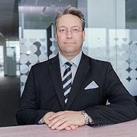 Man in a suit with folded hands sitting in front of a desk