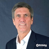 Porträtfoto von Hector Midolo, einem Mann mit grauen Haaren in einem schwarzen Anzug und einem schlauen Lächeln.