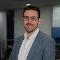 Porträt eines Mitarbeiters im Büro Lächelnder Mitarbeiter mit Brille in grauem Sakko und weißem Hemd in einem modernen Bürogebäude