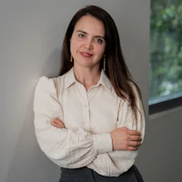 Professional portrait of a female employee Smiling woman in a light blouse and dark trousers stands with folded arms in front of a wall in the office.