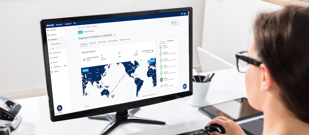 A Woman with Glasses sitting at a Desk looking at the Monitor Screen with the Röhlig Realtime Shipping Map.