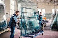 Two man pushing a tilting glass carrier with four glass panes in a production area.