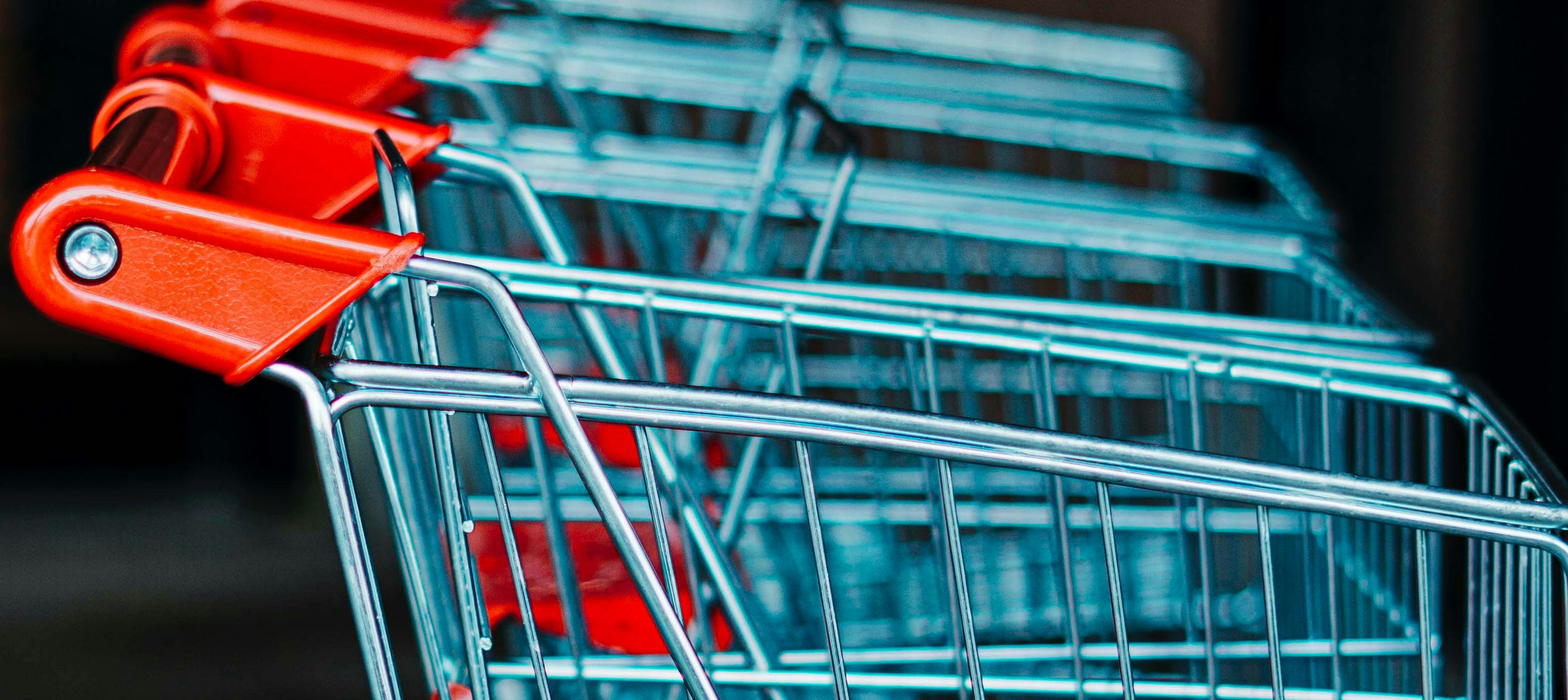 A line of silver shopping carts with red handles and a red toddler seats.