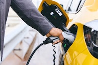 A person in a grey jacket is putting a charging plug in a yellow electronic car.